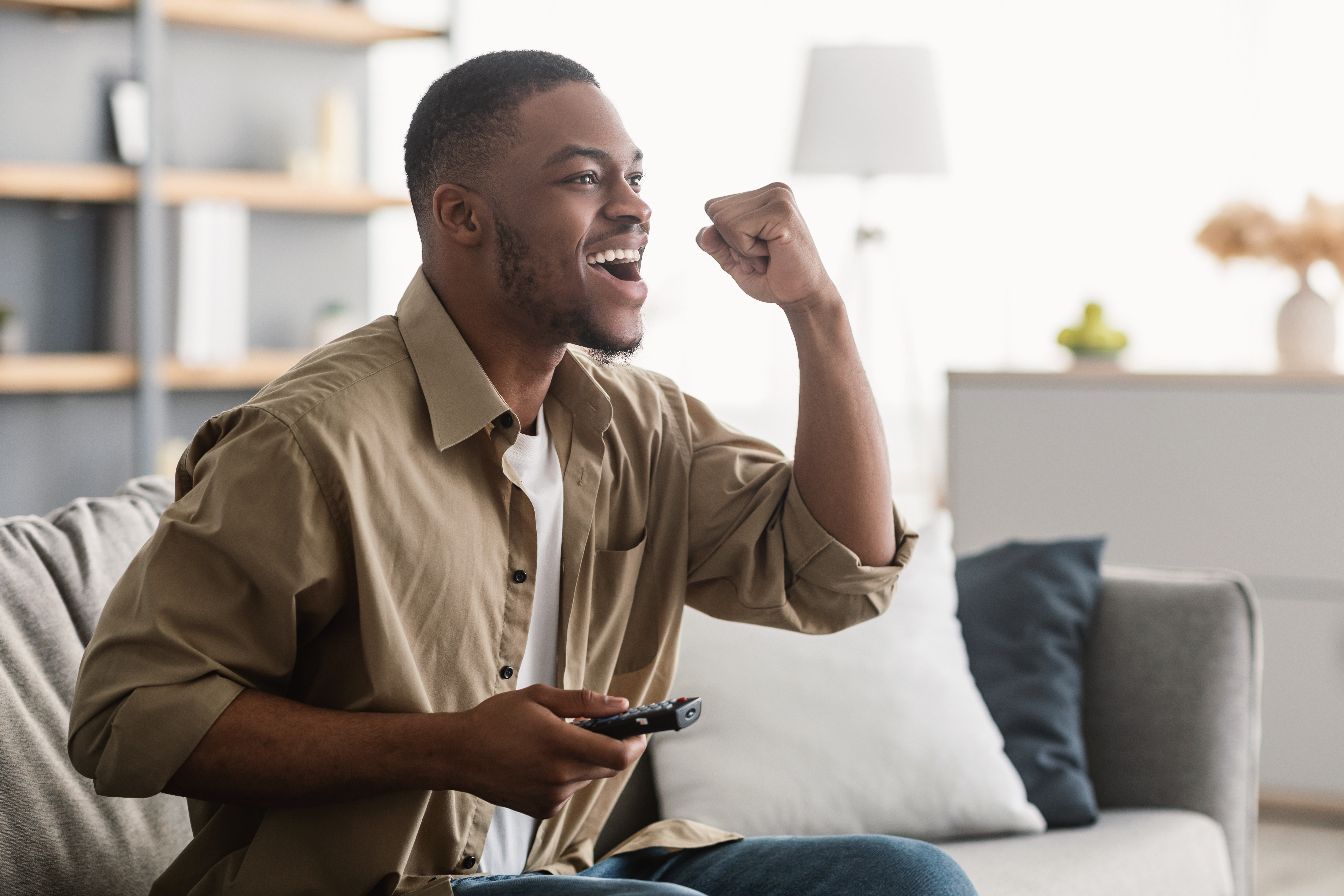 a man watching tv and cheering with a remote in his hand