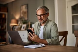 person with laptop open on table using phone