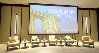 A screen with the title "CTS Summit @ CABSAT" with 5 chairs on a stage