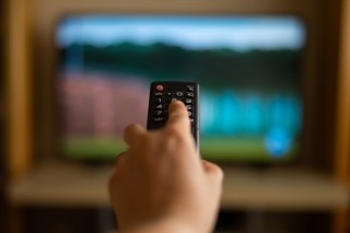 a hand holding a tv remote pointed at a tv