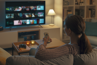 a woman watching tv and holding the tv remote pointed at the tv