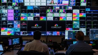 newsroom with tons of tv screens with lots of comcast logos on the screens