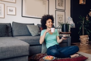 woman sitting on the floor with a cup of coffee and pointing a remote at a tv