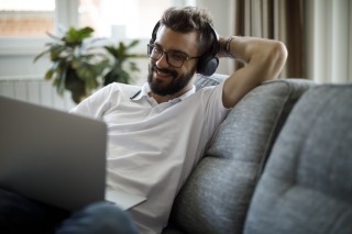 a man with headphones on smiling at his laptop