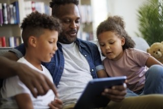 father watching tv on a tablet with his two children