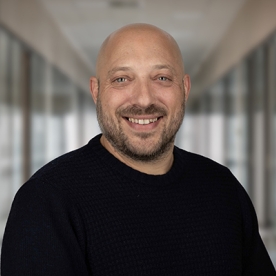 Guy Spivack headshot - bald man with beard in a black shirt