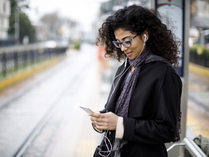 woman wearing coat and scarf on phone at train station outside