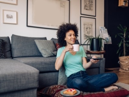 woman sitting on the floor with a cup of coffee and pointing a remote at a tv