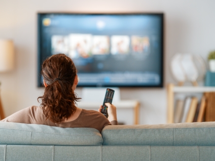woman watching and pointing a remote at a television